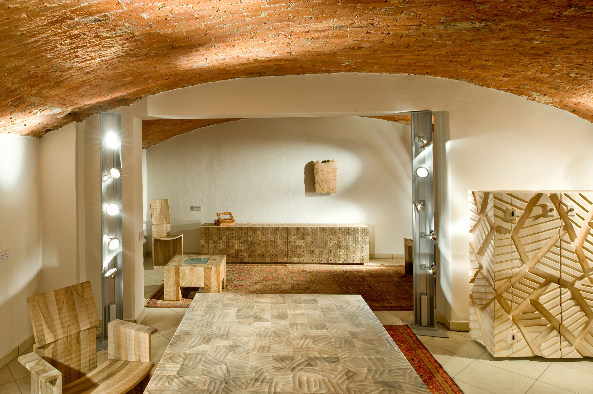 (background) Moissac sideboard in Italian walnut, (centre) Navarra coffe table in Italian walnut, Tanzio high-back chair in Italian walnut. (foreground) Dolmen cabinet in linden, Gaudenzio armchair in Italian walnut.